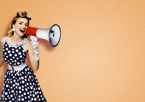 Portrait image of beautiful woman holding mega phone, shout, saying, advertising. Pretty girl in black pin up style dress with mega phone loudspeaker. Isolated latte beige background. Big sales ad.