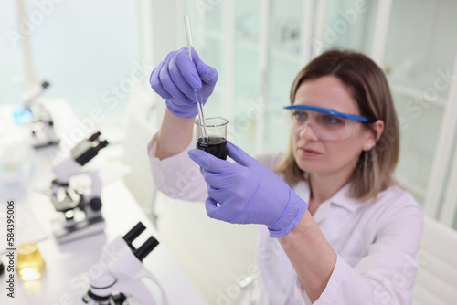 Focused scientist in goggles mixes black liquid in glassware © megaflopp