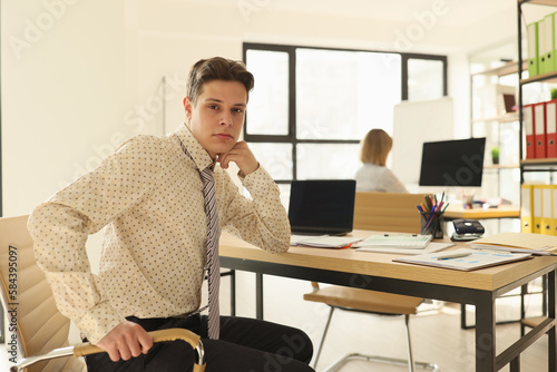 Successful manager sits at table in office looking in camera