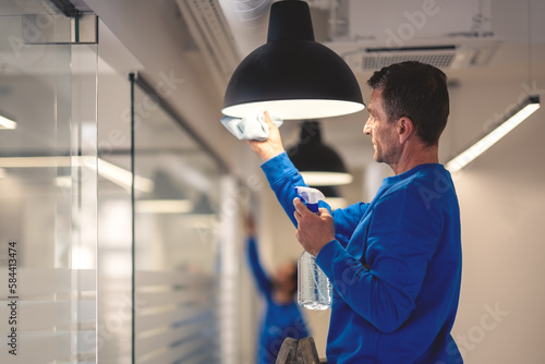 Professional hygiene maintenance. A cleaner cleans the chandelier in the office while in the background another cleaner washes the glass panels