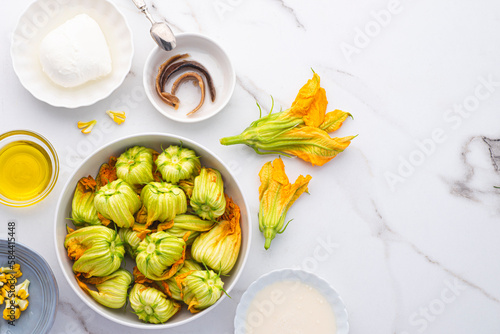  Blossoms flowers zucchini (Courgette, Squash Flowers) or Fiori di zucca and ingredients for frying with mozzarella or others cheese and salted anchovy on the white marble background, copy space photo