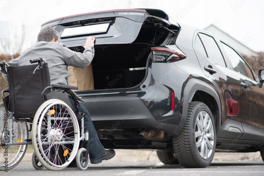 Person with a physical disability puts purchases in the trunk of a car in a supermarket parking lot Person with a physical disability puts purchases in the trunk of a car in a supermarket parking lot