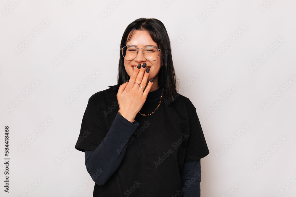 Cute young woman wearing black chuckles while holding hand on her lips. Cute young woman wearing black chuckles while holding hand on her lips.
