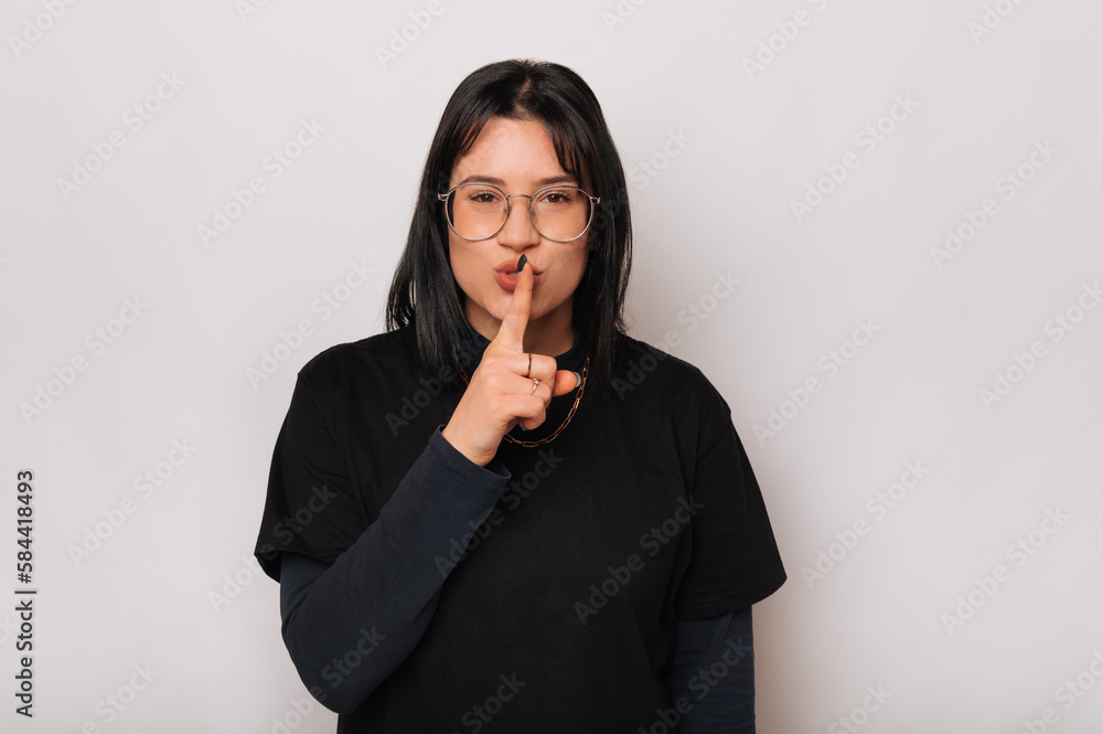 Young cute woman wearing black is holding finger on the lips for silence. Young cute woman wearing black is holding finger on the lips for silence.
