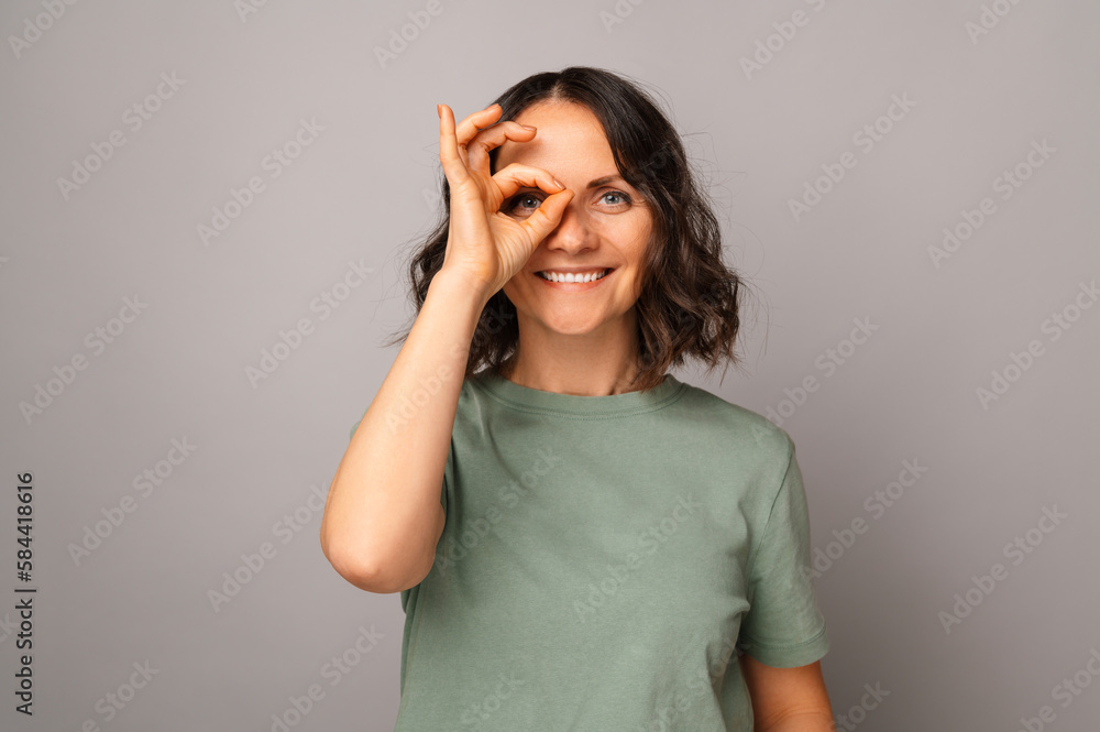 Cheerful mid age woman is making ok gesture over her eye while smiling. Cheerful mid age woman is making ok gesture over her eye while smiling.