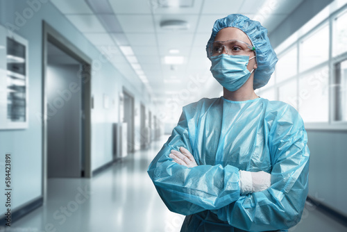 Shot of surgeon woman posing with crossed arms against corridor of modern hospital.