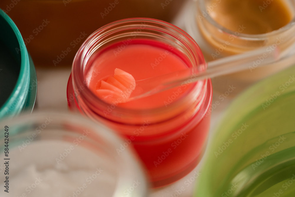 Red plastic jar and spoon with lip balm product close up. Health and skin care morning routine. Selective focus. Red plastic jar and spoon with lip balm product close up. Health and skin care morning routine. Selective focus.
