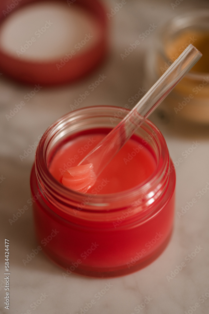 Red plastic jar and spoon with lip balm product close up. Health and skin care morning routine. Selective focus. Red plastic jar and spoon with lip balm product close up. Health and skin care morning routine. Selective focus.