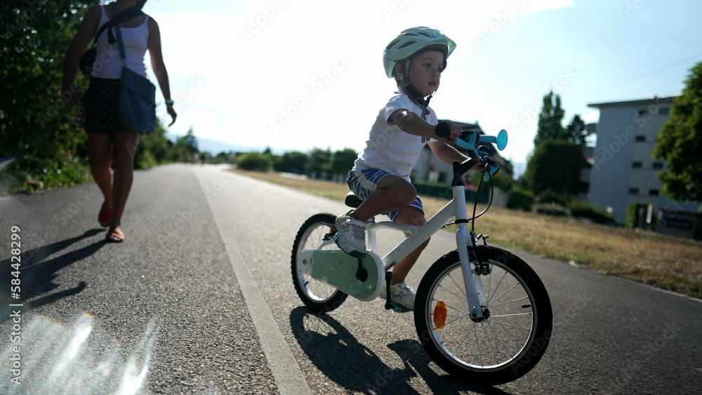 Obraz premium One active little boy riding bicycle outdoors in urban bike road. Little kid wearing a protective helmet staying in balance. Handheld slow motion footage