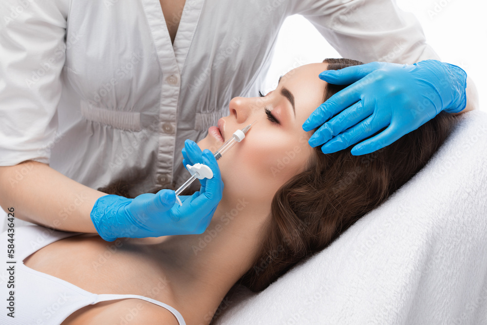 Cosmetologist does injections for lips augmentation and anti wrinkle in the nasolabial folds of a beautiful woman. Women's cosmetology in the beauty salon. Cosmetologist does injections for lips augmentation and anti wrinkle in the nasolabial folds of a beautiful woman. Women's cosmetology in the beauty salon.