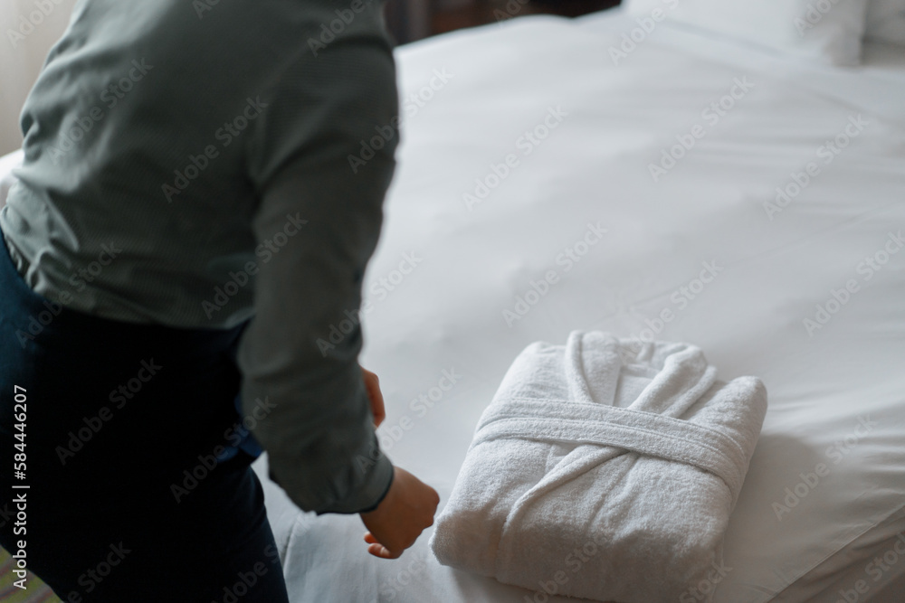 Housekeeper in uniform is folding white coat preparing luxury hotel room for guests cleaning and travel concept