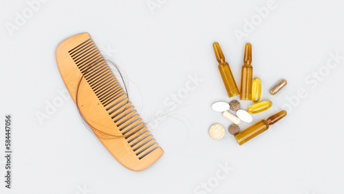 Cosmetic ampoules with serum and vitamins for hair growth  restoration beauty hair. Wooden comb with hair loss on a gray background. Hair loss  baldness problem concept. Self-care  wellness. Flat lay