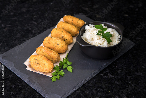 Bolinhos de bacalhau, very famous in Portuguese gastronomy. Fried dumpling, cod dumpling, fish, salted cod fritters, bacalao bunuelos. Codfish cake served with white rice on a dark background. photo