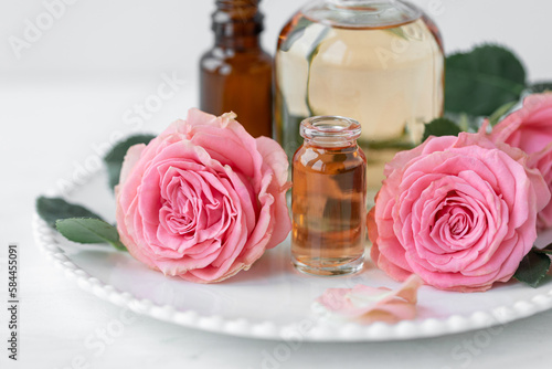 Aromatherapy. Concept of pure organic essential rose oil. Elixir with plant based floral or herbal ingredients. Pink flowers extract. Spa atmosphere with candle, towel. White background