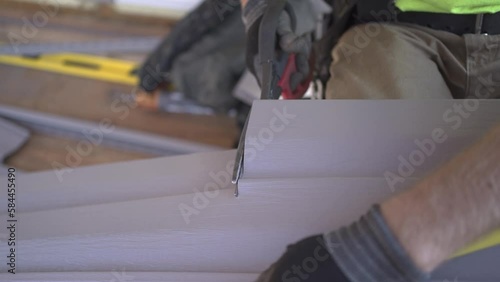 Finishing the house with siding: preparatory work. A man cuts gray siding with construction scissors.