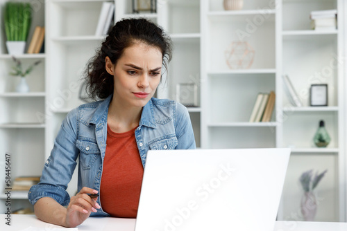 A young curly-haired brunette student sits at a table and uses a laptop for learning. Online school, remote work, programmer or manager. The concept of remote work or learning