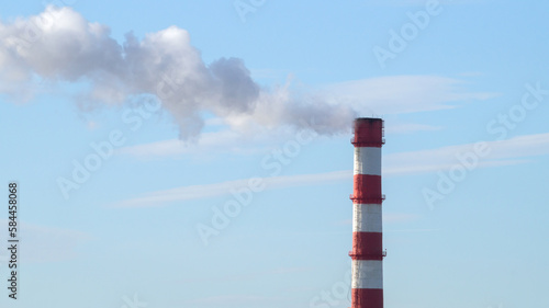 A factory chimney with red stripes smokes against a blue sky.