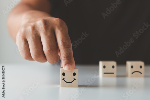 customer services best excellent business rating experience. satisfaction review survey concept. Close-up of the customer s hand choosing a smile face and blurred sad face icon on the wood cube block.