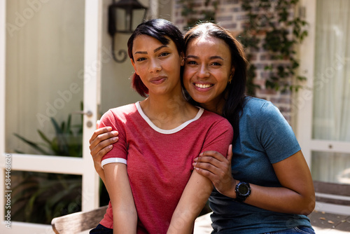 Portrait of happy biracial sisters looking at camera and embracing