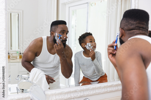 Happy african american father and son shaving beard in bathroom