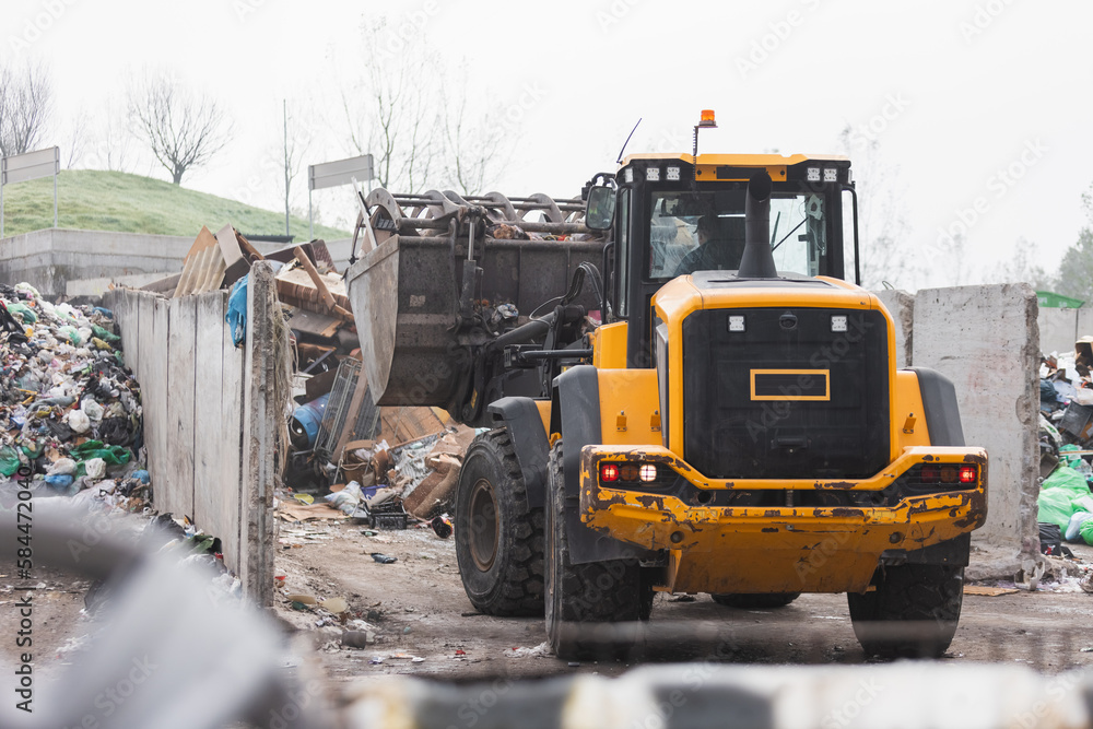 Obraz premium Heavy construction machine, front end loader moving along recycling center area, close up view. Waste management industry concept.