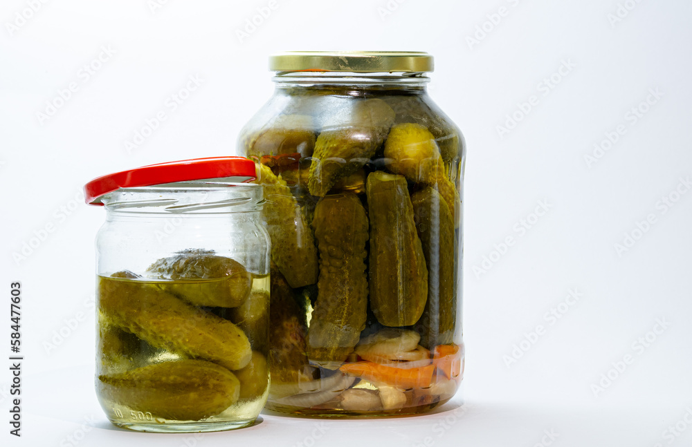 Two jars of canned pickles, on a white background, one jar is closed, the second is open, the lid is next to the jar. Two jars of canned pickles, on a white background, one jar is closed, the second is open, the lid is next to the jar.