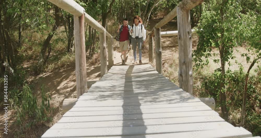 Happy african american couple wearing backpack, hiking on boardwalk in forest, slow motion Happy african american couple wearing backpack, hiking on boardwalk in forest, slow motion