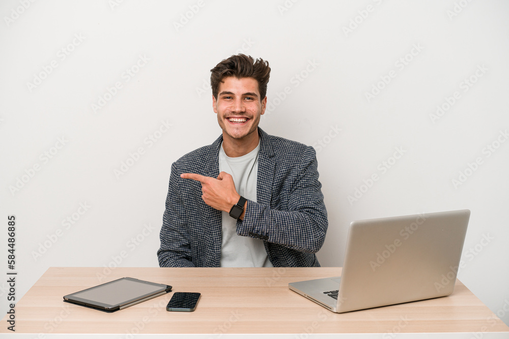 Young entrepreneur man working with a laptop isolated smiling and pointing aside, showing something at blank space. Young entrepreneur man working with a laptop isolated smiling and pointing aside, showing something at blank space.