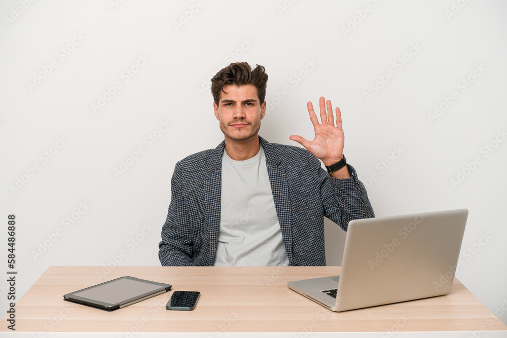Young entrepreneur man working with a laptop isolated smiling cheerful showing number five with fingers. Young entrepreneur man working with a laptop isolated smiling cheerful showing number five with fingers.