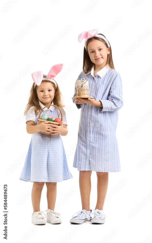 Little girls in bunny ears with Easter eggs and cake on white background Little girls in bunny ears with Easter eggs and cake on white background