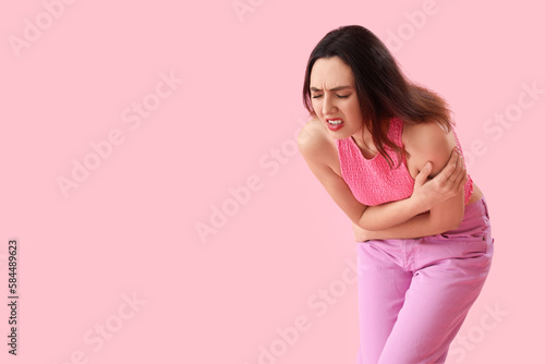 Young woman suffering from menstrual cramps on pink background