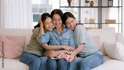 Happy time May Mother day cuddle hug care love face to face kiss cheek to mature mum. Asia middle aged old mom adult people smile enjoy receive gift flower from young child sitting at home sofa relax.