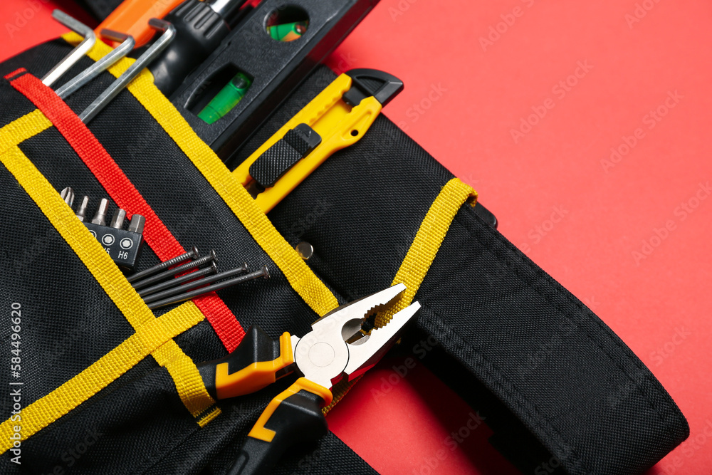 Belt with pliers and tools on red background Belt with pliers and tools on red background