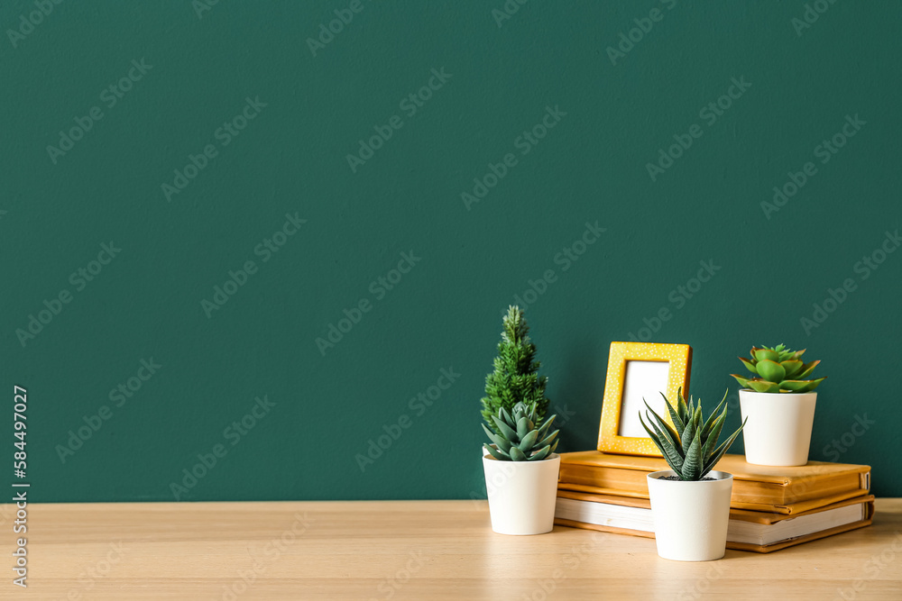 Artificial plants with frame and books on table near green wall Artificial plants with frame and books on table near green wall