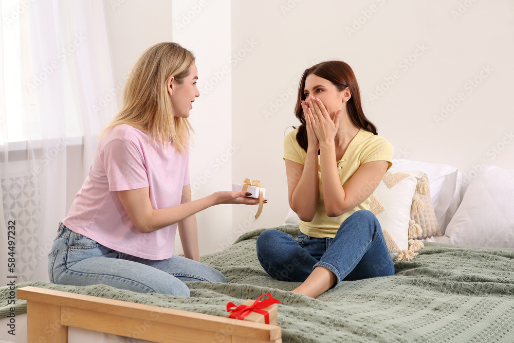 Smiling young women presenting gifts to each other on bed at home