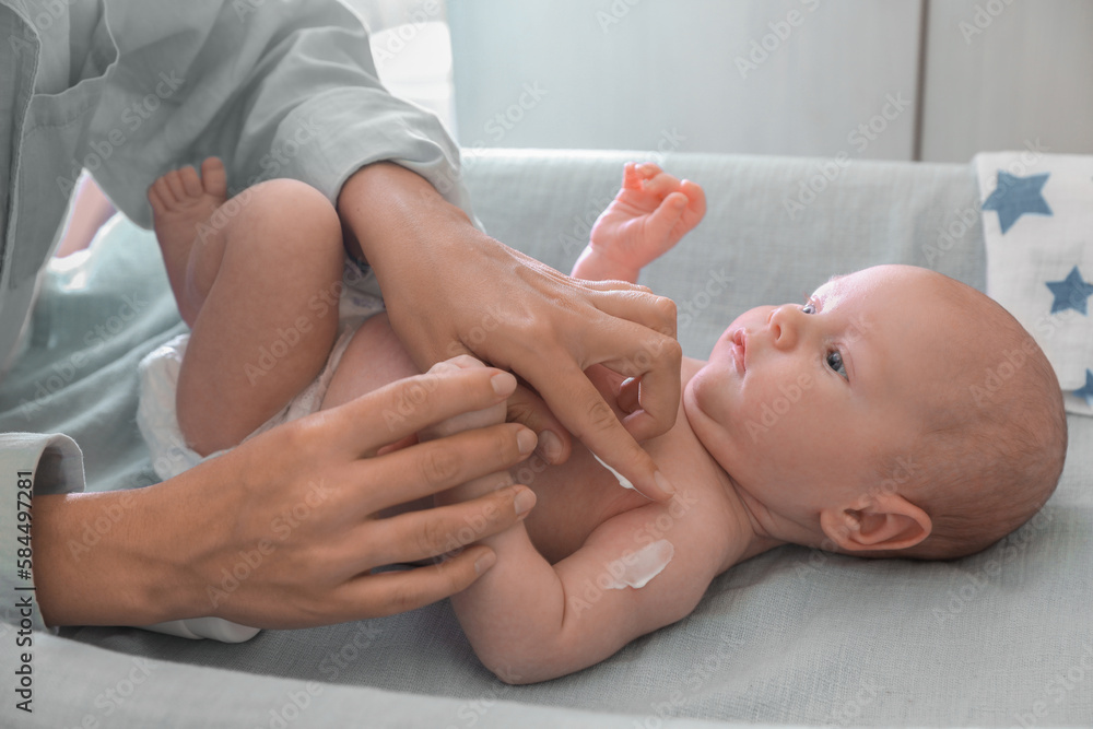 Mother applying moisturizing cream onto baby`s arm on changing table indoors, closeup Mother applying moisturizing cream onto baby`s arm on changing table indoors, closeup
