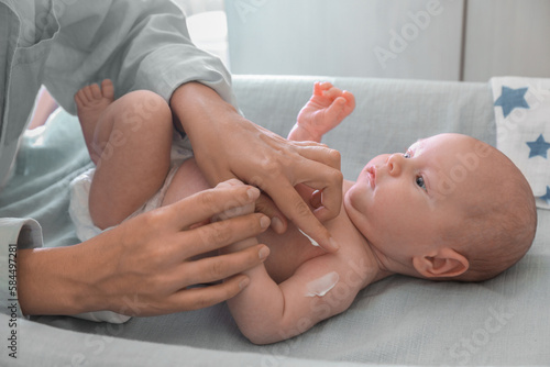 Mother applying moisturizing cream onto baby`s arm on changing table indoors, closeup