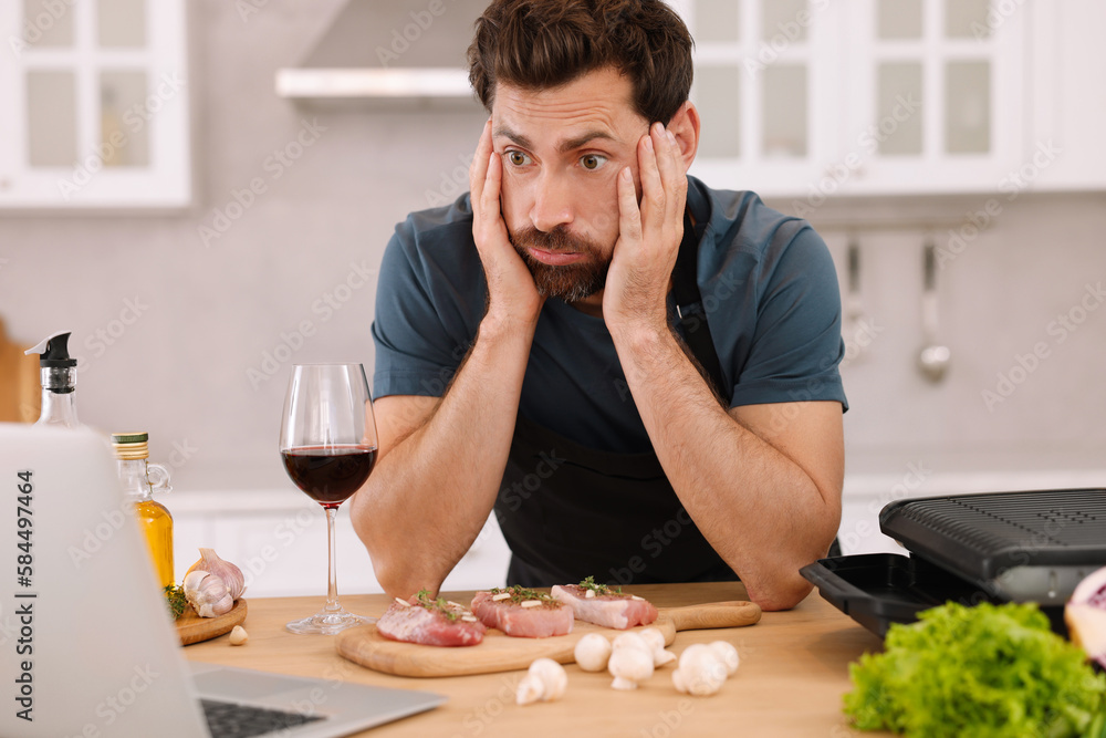 Man making dinner while watching online cooking course via laptop in kitchen Man making dinner while watching online cooking course via laptop in kitchen