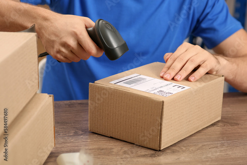 Post office worker with scanner reading parcel barcode at counter, closeup