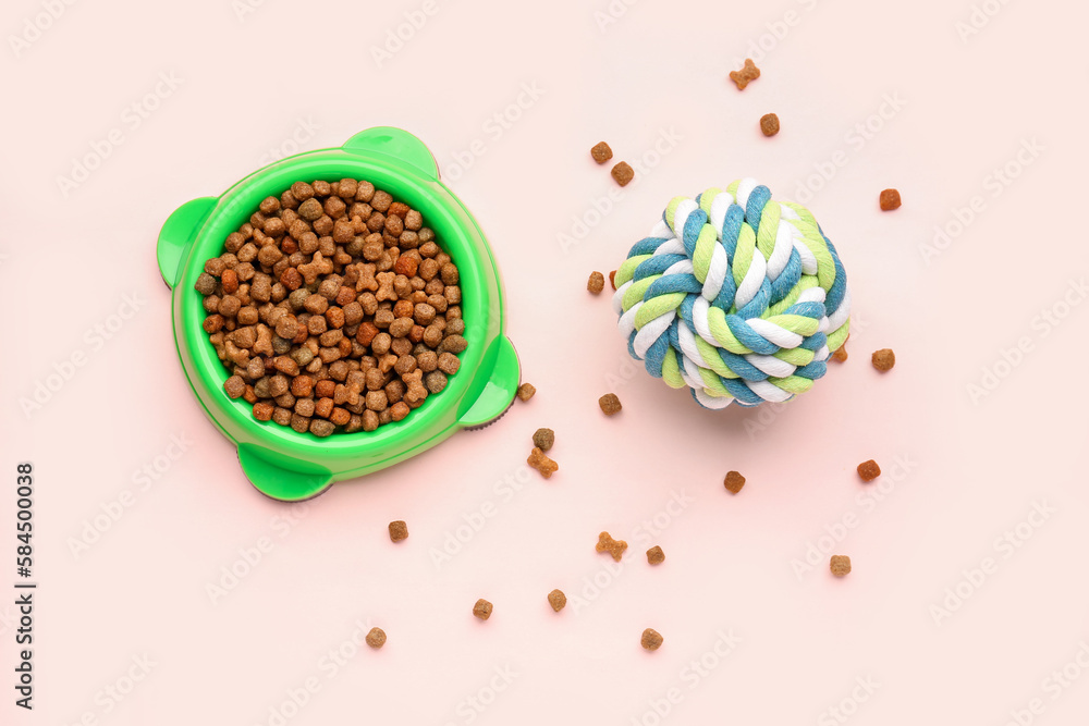 Bowl of dry pet food and toy ball on pink background Bowl of dry pet food and toy ball on pink background