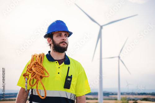 Bearded technician engineer of windmill and renewable energy industry working and looking the turbine to reapir and fix the problems wearing helmet an saftery vest. Electricty power concept. High photo