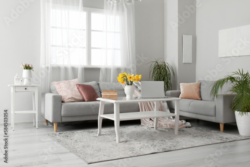 Interior of living room with modern laptop and flower vase on coffee table near sofas