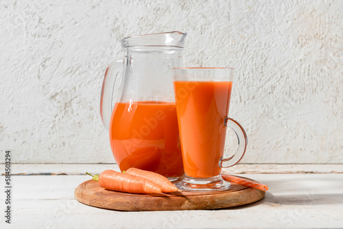 Glass and jug of fresh carrot juice on white grunge table