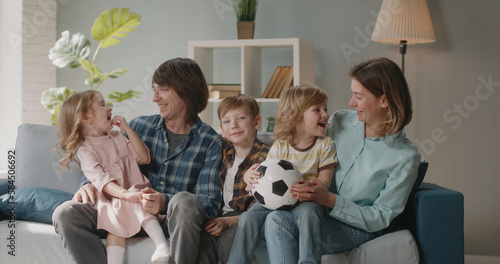 Portrait shot of happy large caucasian family of five sitting on couch at home together, positively smiling and looking at camera - happy family, real people 