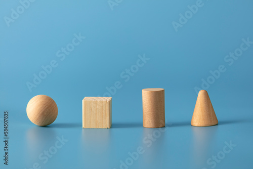 Geometric wood shapes on blue background. Sphere, cube, cylinder and a cone. 