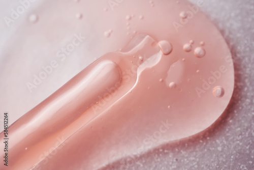 A pipette with a viscous pink cosmetic lies in a drop.