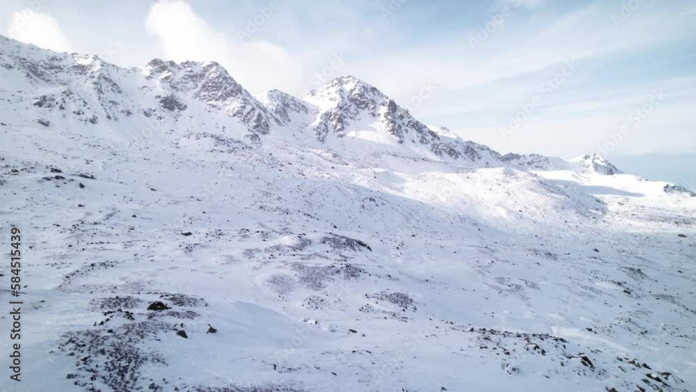 Aerial view of snow covered mountain landscape on a sunny day with clouds rolling behind in Fluela Pass, Switzerland. Aerial view of snow covered mountain landscape on a sunny day with clouds rolling behind in Fluela Pass, Switzerland.