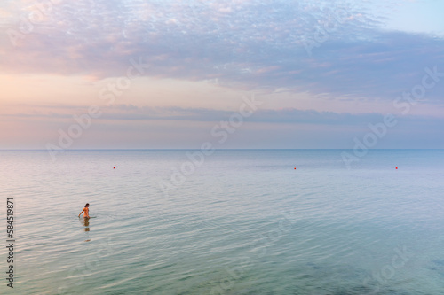Rear view of a woman in brown swimwear going into the sea on the beach at sunrise