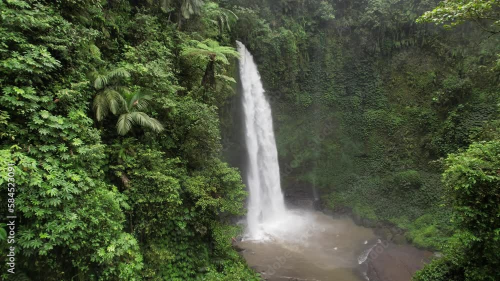 Beautiful big waterfall in green canyon, camera fly towards rushing water. Powerful stream splash down in pond, white spray fly around. Natural landmark of central Bali, one of biggest waterfalls Beautiful big waterfall in green canyon, camera fly towards rushing water. Powerful stream splash down in pond, white spray fly around. Natural landmark of central Bali, one of biggest waterfalls