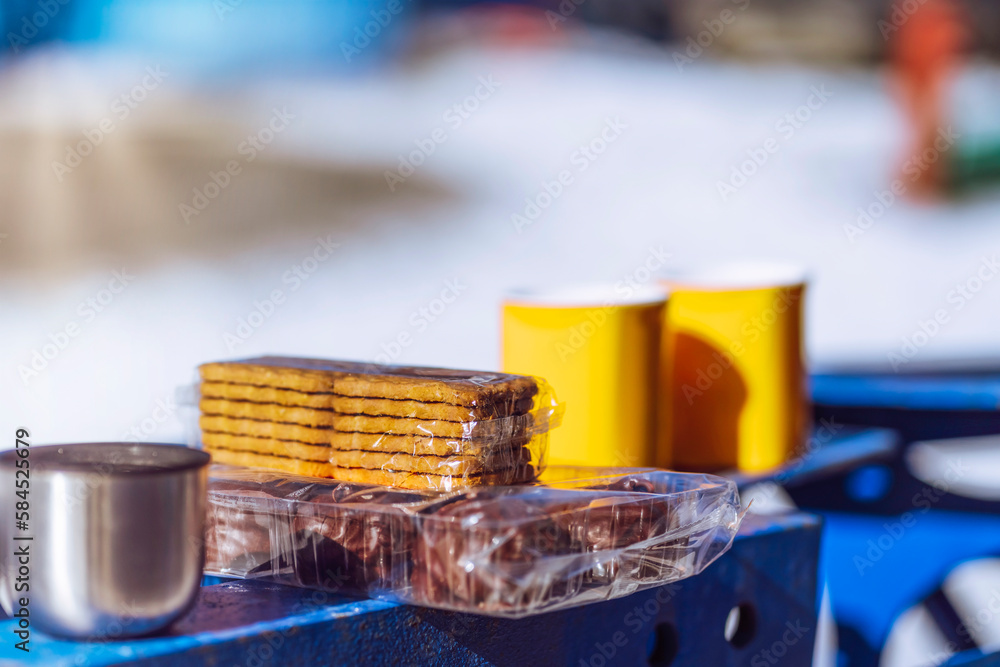 two yellow mugs with a hot drink and cookies with marshmallows on a metal structure on a winter day two yellow mugs with a hot drink and cookies with marshmallows on a metal structure on a winter day